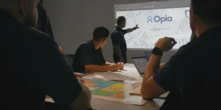 Equipo de profesionales reunidos en una sala de juntas viendo una presentación de proyectos proyectada en la pared.