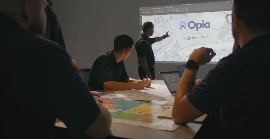 Equipo de profesionales reunidos en una sala de juntas viendo una presentación de proyectos proyectada en la pared.