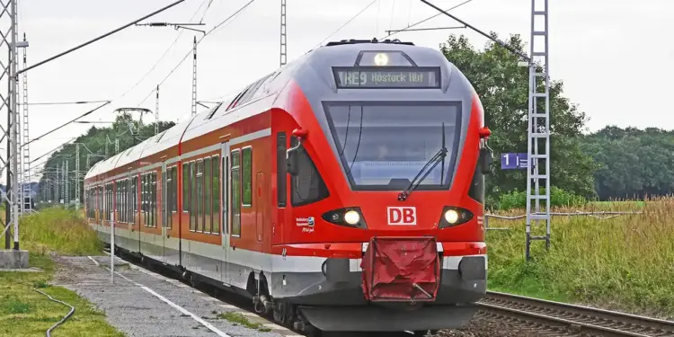 Tren regional de pasajeros de color rojo y gris circulando por vías férreas en una zona rural.