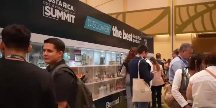 Asistentes y expositores en un evento de negocios y comercio con estantes iluminados y un cartel de la cumbre.