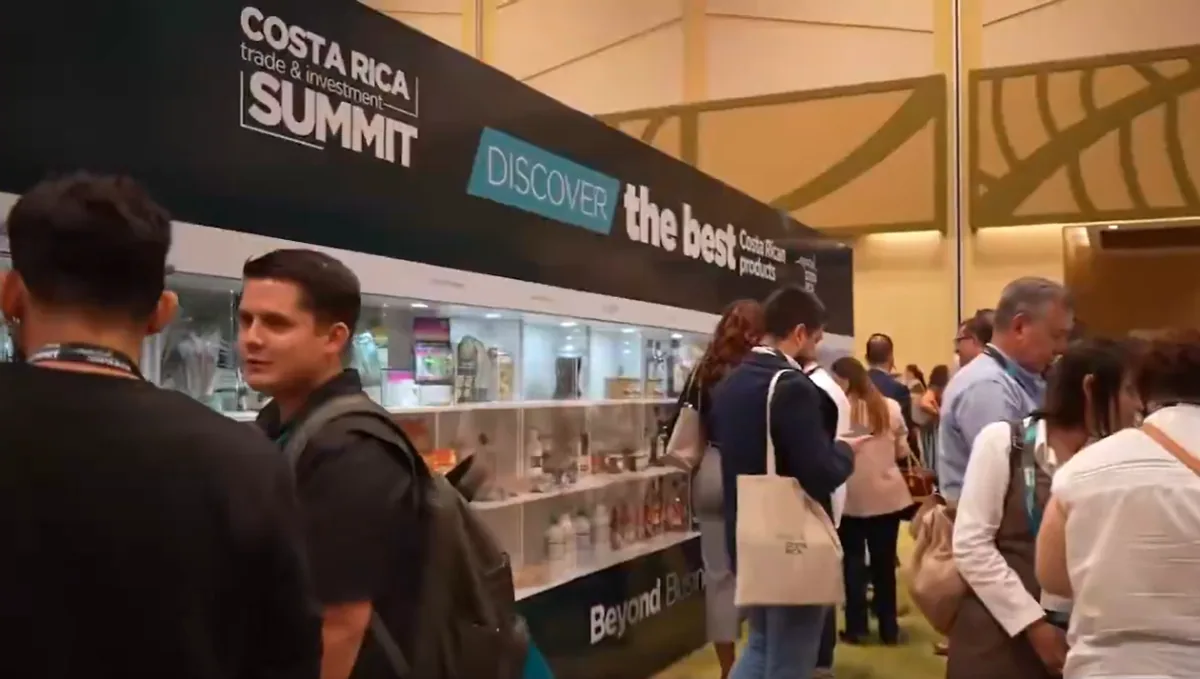Asistentes y expositores en un evento de negocios y comercio con estantes iluminados y un cartel de la cumbre.