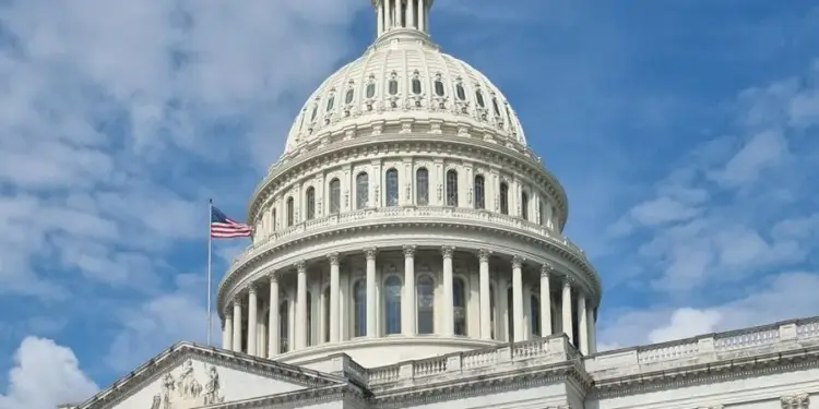 Cúpula del Capitolio de estilo neoclásico con la bandera de Estados Unidos flameando en un cielo azul.