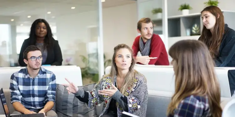 Grupo diverso de profesionales en una reunión de negocios, discutiendo ideas en un entorno colaborativo de oficina moderna. Una mujer gesticula mientras habla.