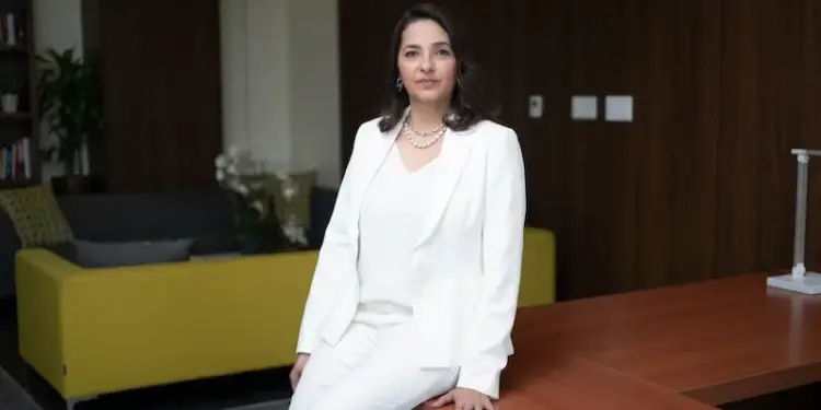Profesional femenina con traje sastre blanco sentada en un escritorio de madera en una oficina corporativa.