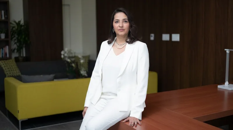 Profesional femenina con traje sastre blanco sentada en un escritorio de madera en una oficina corporativa.
