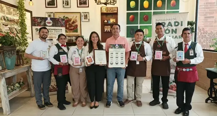 Ocho profesionales, hombres y mujeres, posan con certificados y productos de café. Visten uniformes y ropa de negocios, celebrando logros empresariales y calidad.