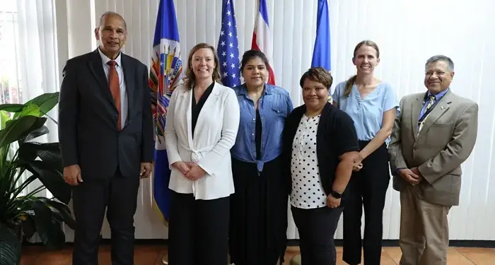 Siete profesionales, incluyendo mujeres y hombres, en un entorno oficial con banderas de fondo, simbolizando colaboración.