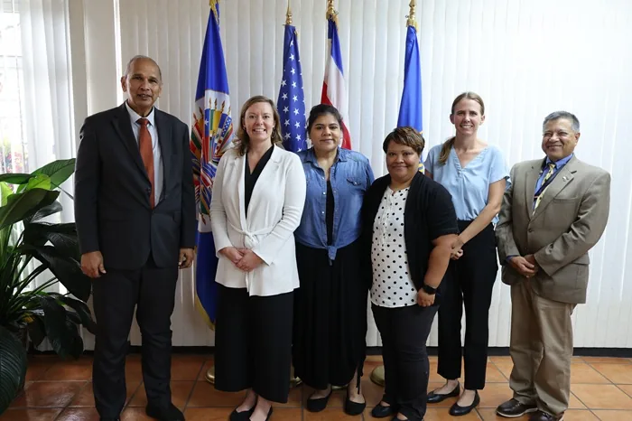 Siete profesionales, incluyendo mujeres y hombres, en un entorno oficial con banderas de fondo, simbolizando colaboración.