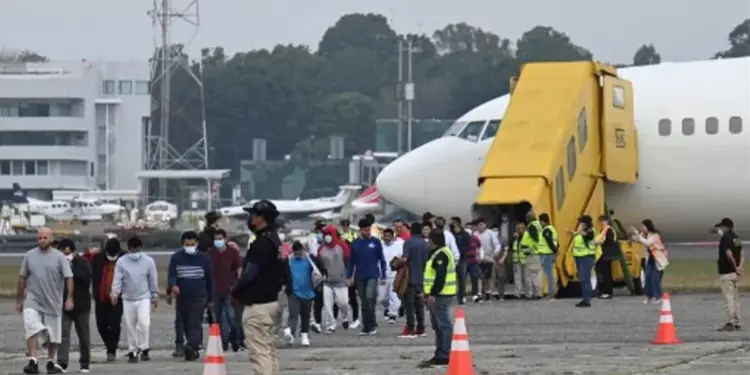 Grupo de personas caminando por la pista de un aeropuerto cerca de un avión comercial con una escalera amarilla.