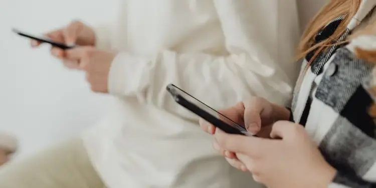 Dos personas utilizando sus teléfonos inteligentes cerca de una pared blanca.