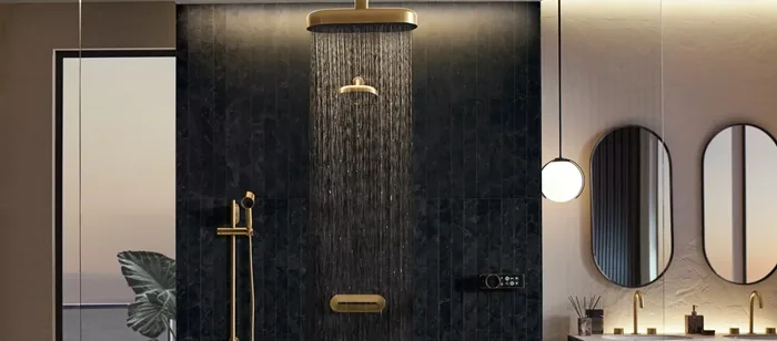 Baño de lujo moderno con ducha de lluvia dorada y grifería a juego. Pared de azulejos oscuros, espejos ovalados y lavabos dobles.
