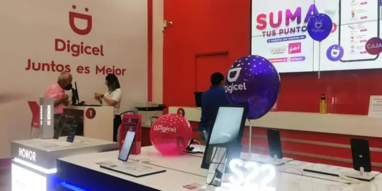 Interior de una tienda Digicel con empleados atendiendo a un cliente. Se exhiben smartphones y una pantalla muestra promociones de puntos.