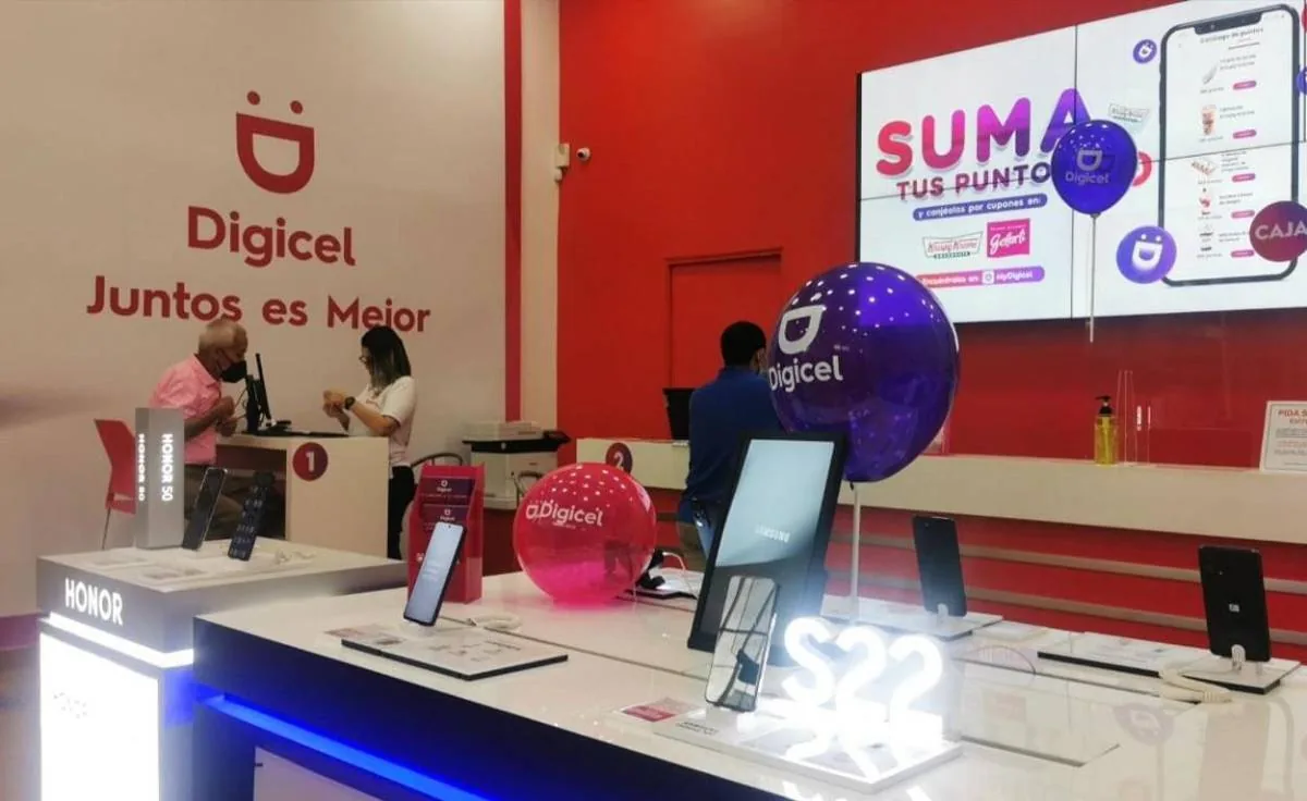 Interior de una tienda Digicel con empleados atendiendo a un cliente. Se exhiben smartphones y una pantalla muestra promociones de puntos.