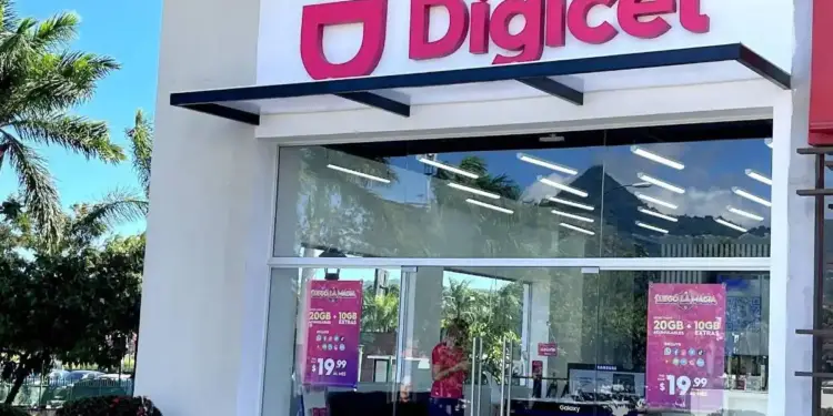 Fachada de una tienda Digicel con letrero rosa brillante y fachada de vidrio. Se aprecian ofertas de planes de datos y un empleado dentro.