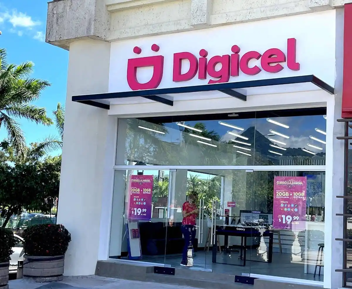 Fachada de una tienda Digicel con letrero rosa brillante y fachada de vidrio. Se aprecian ofertas de planes de datos y un empleado dentro.
