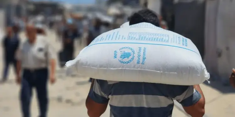 Hombre cargando al hombro un saco blanco de ayuda alimentaria del World Food Programme (WFP) en una calle.