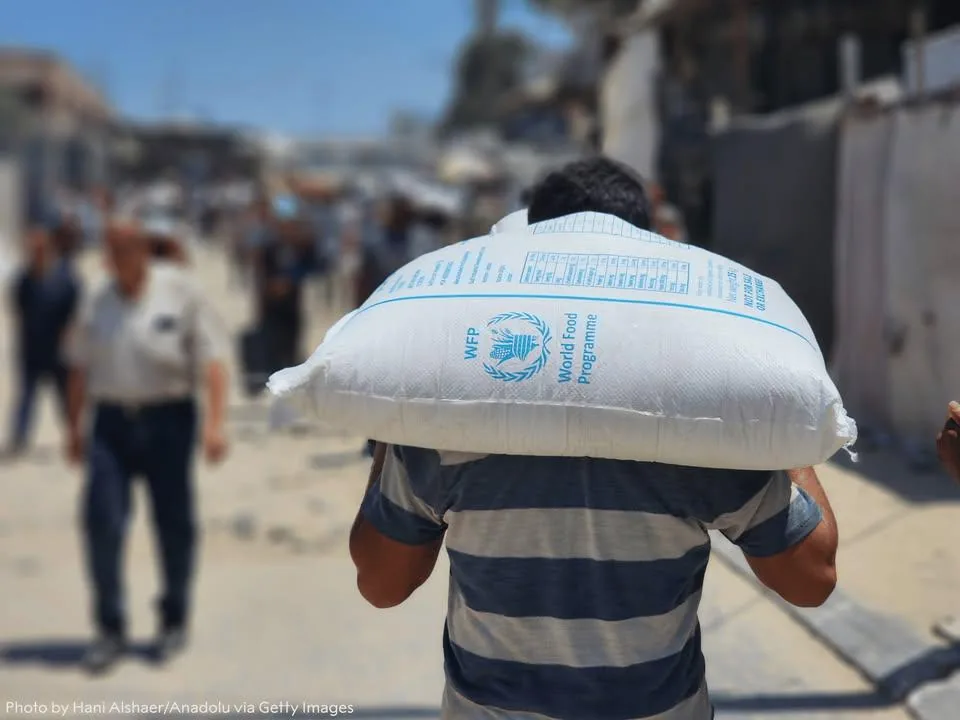 Hombre cargando al hombro un saco blanco de ayuda alimentaria del World Food Programme (WFP) en una calle.