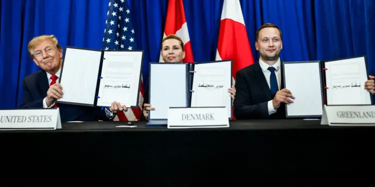 Tres personas sentadas ante una mesa con carteles de United States, Denmark y Greenland mostrando documentos firmados.