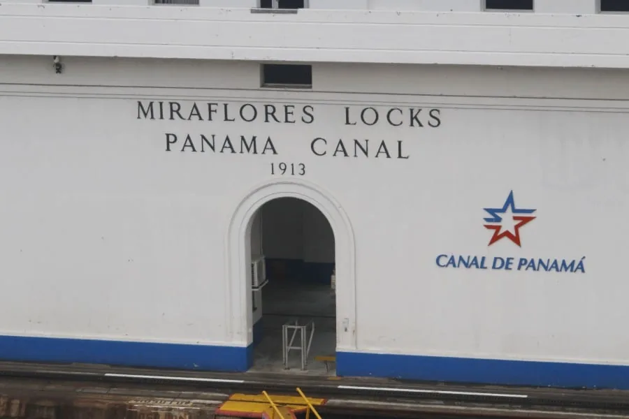 Fachada blanca de un edificio de las esclusas de Miraflores con el texto Canal de Panamá y un logotipo de estrella azul y roja.