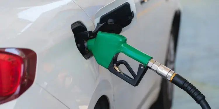 Boquerel verde de gasolina insertado en el tanque de un coche blanco, mostrando el proceso de repostaje. Refleja costos de combustible.