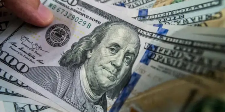 Una mano sosteniendo varios billetes de cien dólares estadounidenses con el retrato de Benjamin Franklin.
