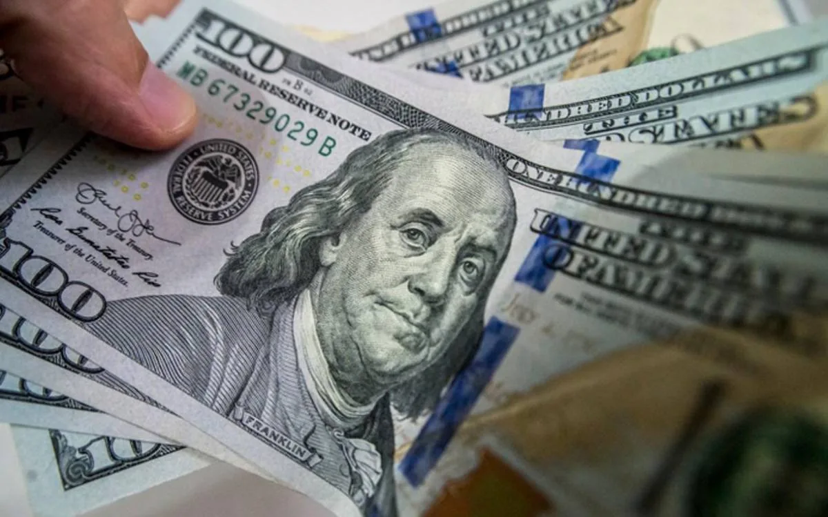 Una mano sosteniendo varios billetes de cien dólares estadounidenses con el retrato de Benjamin Franklin.
