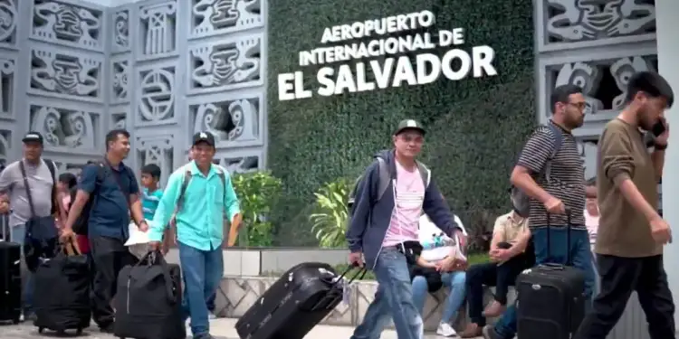 Viajeros caminando con equipaje frente al letrero del Aeropuerto Internacional de El Salvador.