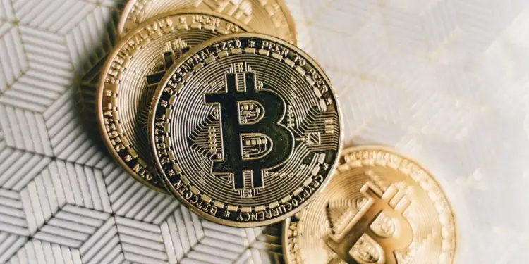 Monedas físicas doradas de bitcoin dispuestas sobre una superficie con patrón geométrico texturizado en tonos claros.