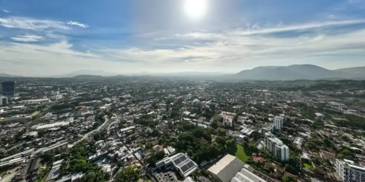 Vista panorámica aérea de una ciudad extensa bajo un cielo brillante con el sol en lo alto.
