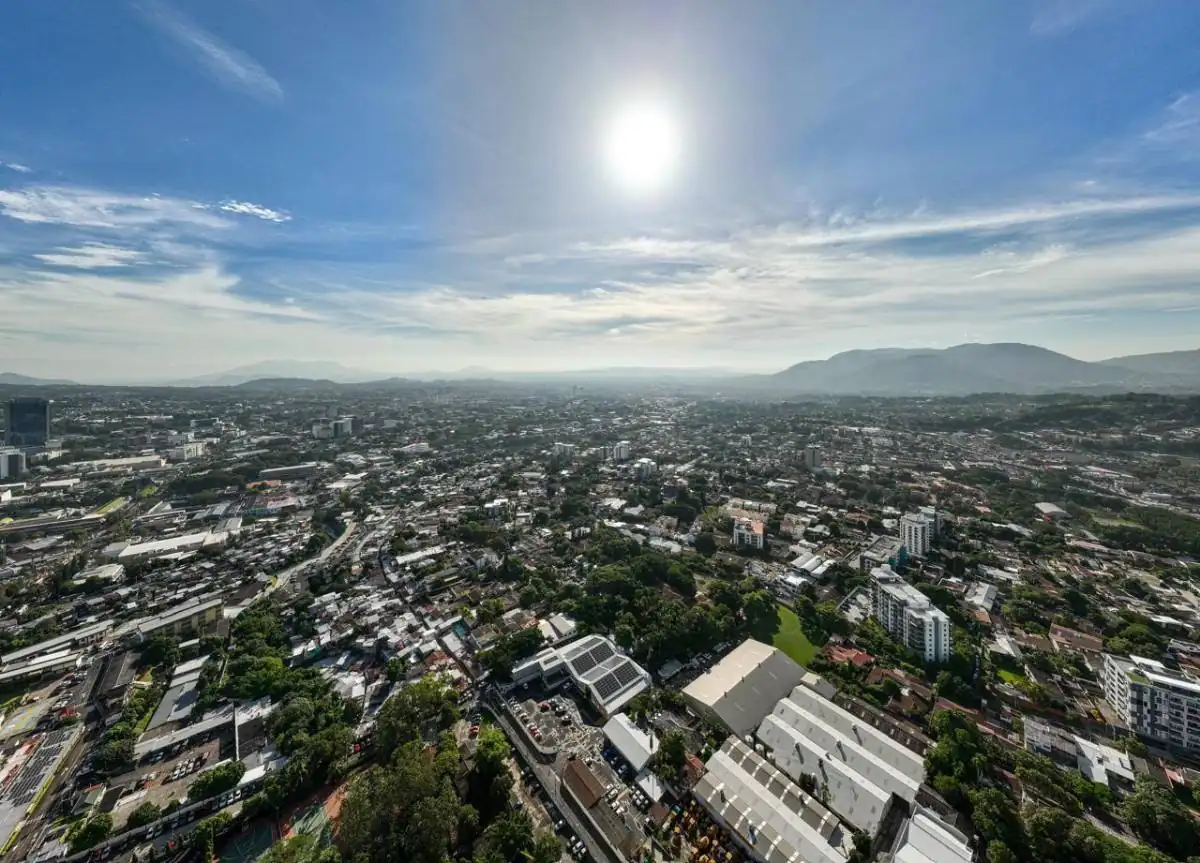 Vista panorámica aérea de una ciudad extensa bajo un cielo brillante con el sol en lo alto.
