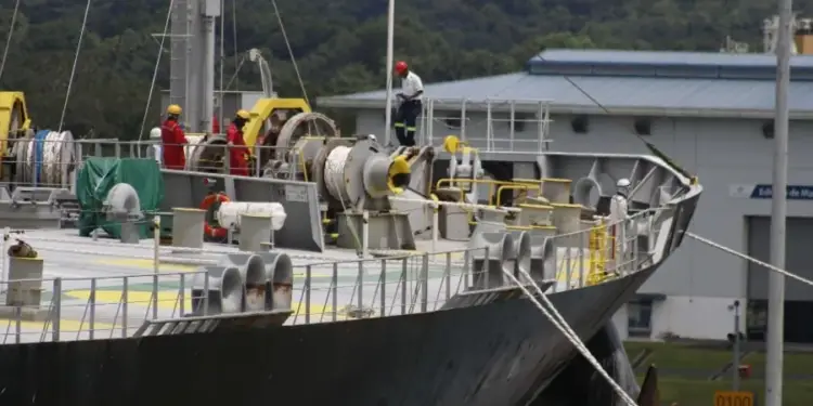 Vista de la cubierta de un gran barco con trabajadores en puerto y equipamiento industrial.