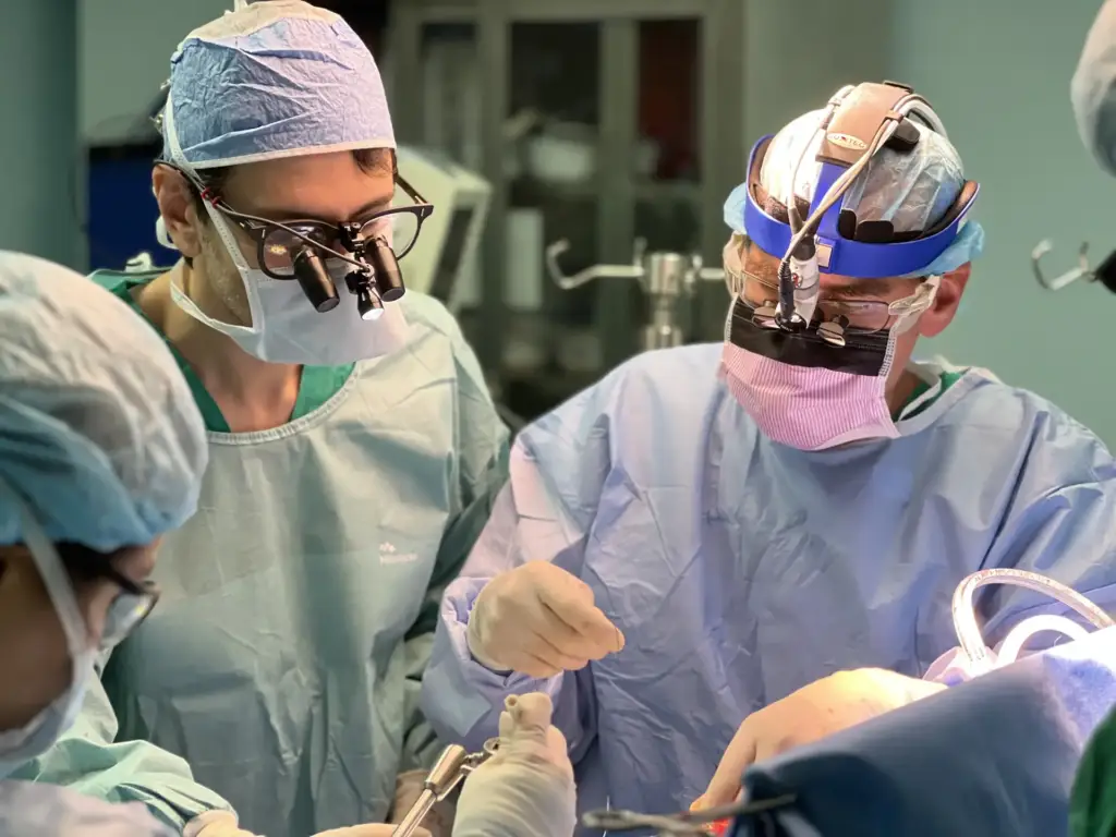 Personal médico con uniforme quirúrgico y lupas especiales realizando una intervención en un quirófano.