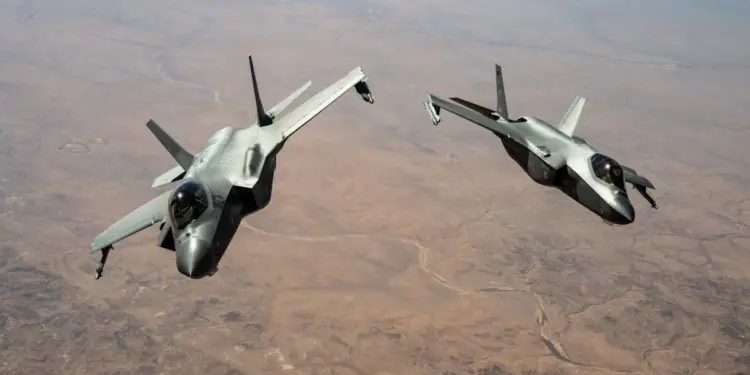 Dos aviones de combate militares modernos volando en formación sobre un paisaje desértico árido.