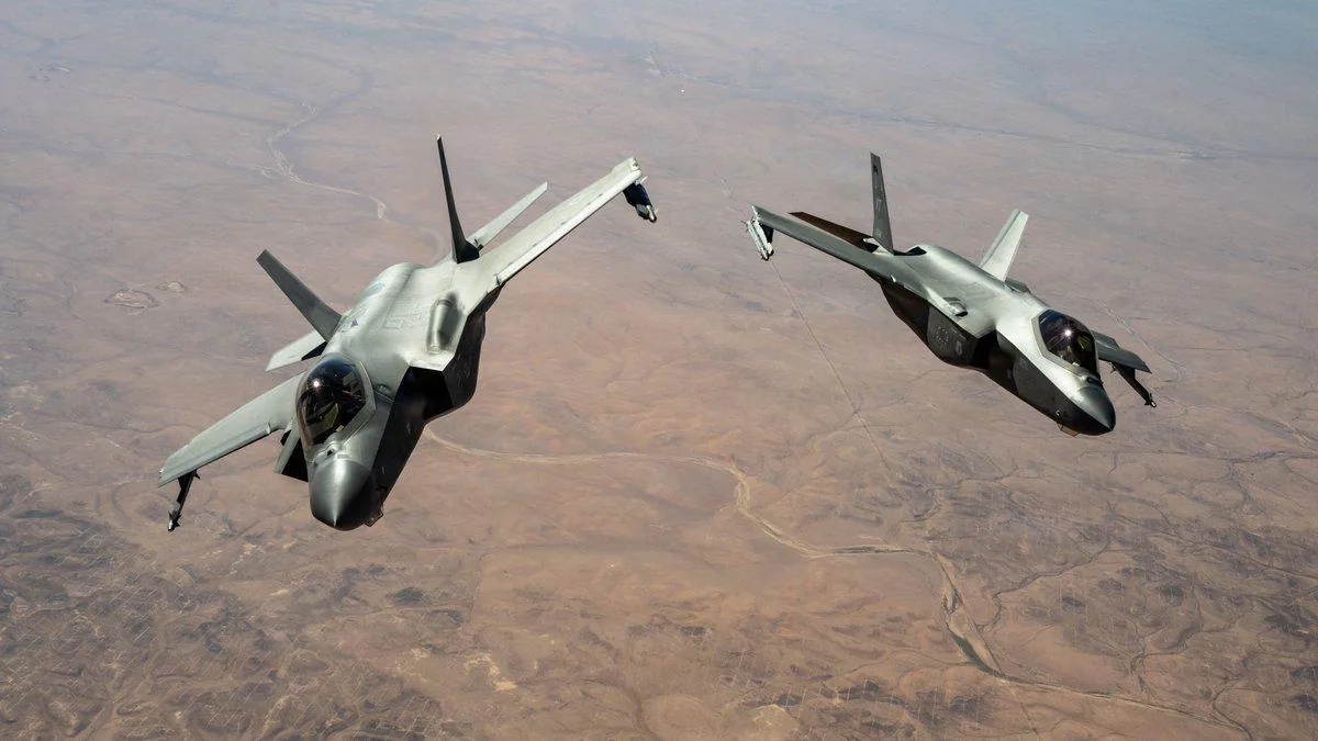 Dos aviones de combate militares modernos volando en formación sobre un paisaje desértico árido.