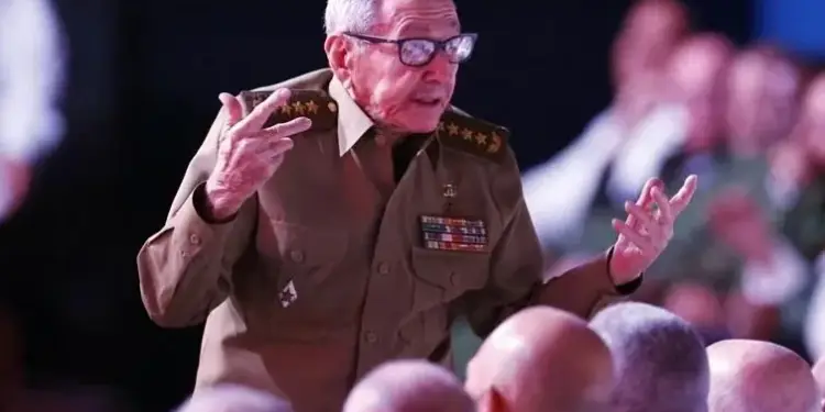 Hombre mayor con uniforme militar y gafas gesticulando frente a una audiencia en un evento público.