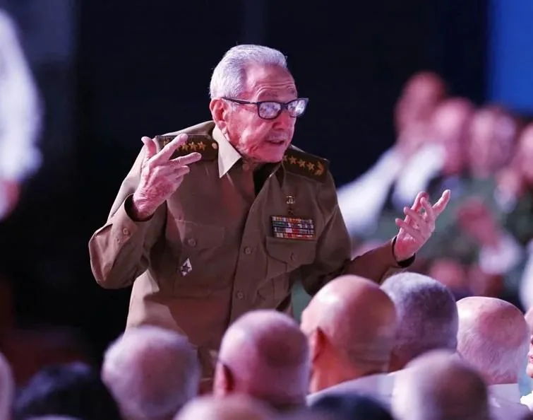 Hombre mayor con uniforme militar y gafas gesticulando frente a una audiencia en un evento público.