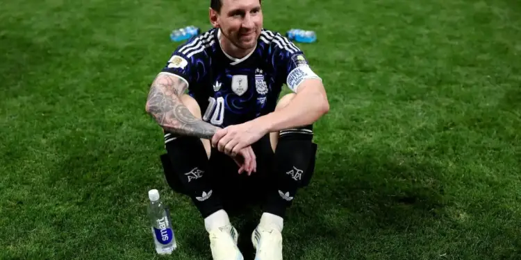 Futbolista sentado en el césped con camiseta deportiva oscura y botellas de agua alrededor