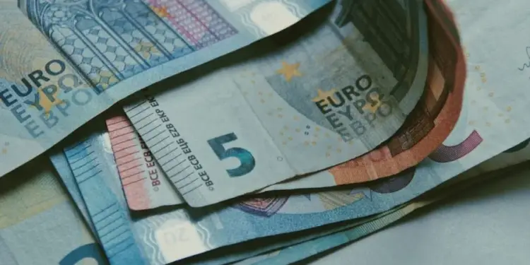 Primer plano de varios billetes de Euro apilados y extendidos, mostrando denominaciones de 5 y 20 euros sobre una superficie clara.