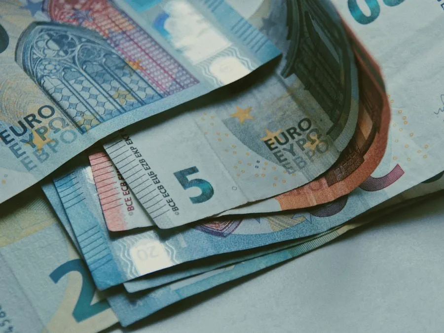Primer plano de varios billetes de Euro apilados y extendidos, mostrando denominaciones de 5 y 20 euros sobre una superficie clara.
