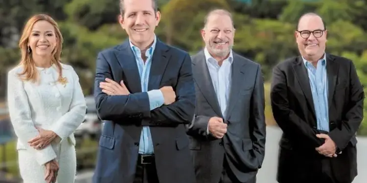 Cuatro profesionales de negocios, una mujer y tres hombres, sonriendo con vestimenta formal al aire libre.
