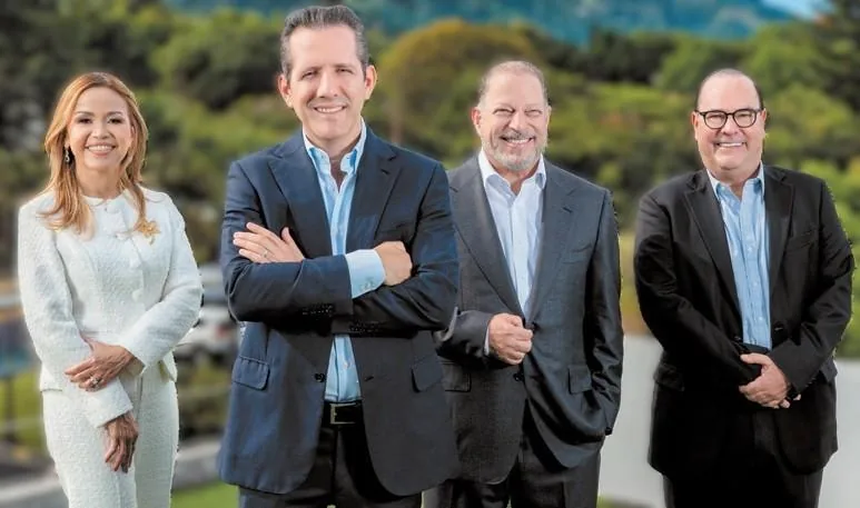 Cuatro profesionales de negocios, una mujer y tres hombres, sonriendo con vestimenta formal al aire libre.