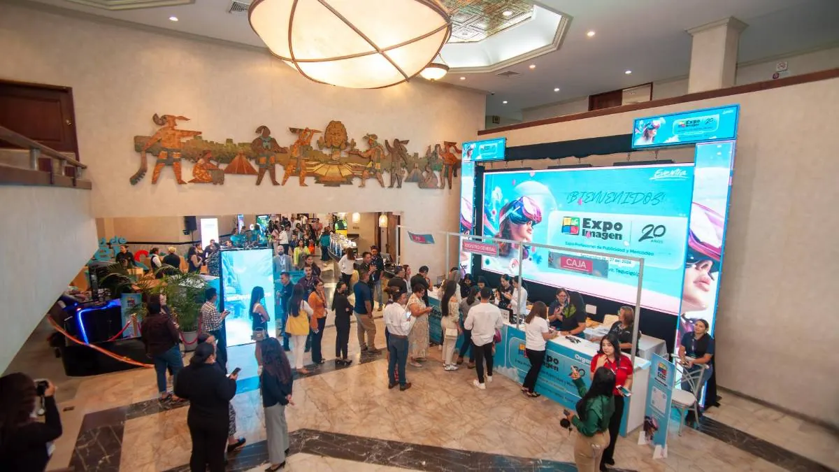 Vista superior de un concurrido vestíbulo de hotel con un mostrador de registro y pantallas LED para un evento de negocios.