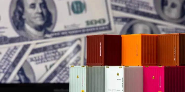 Contenedores de envío en miniatura de colores (rojo, naranja, blanco, rosa) apilados frente a billetes de cien dólares estadounidenses borrosos.