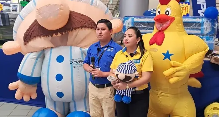 Un hombre y una mujer de pie entre dos grandes botargas inflables en un evento comercial o centro de negocios.