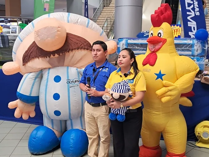 Un hombre y una mujer de pie entre dos grandes botargas inflables en un evento comercial o centro de negocios.