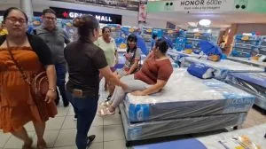 Cliente sentada probando la comodidad de un colchón en una tienda con varias personas observando.
