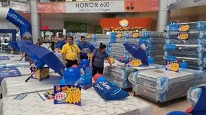 Exhibición de múltiples colchones envueltos en plástico con sombrillas azules y personal atendiendo en un centro comercial.