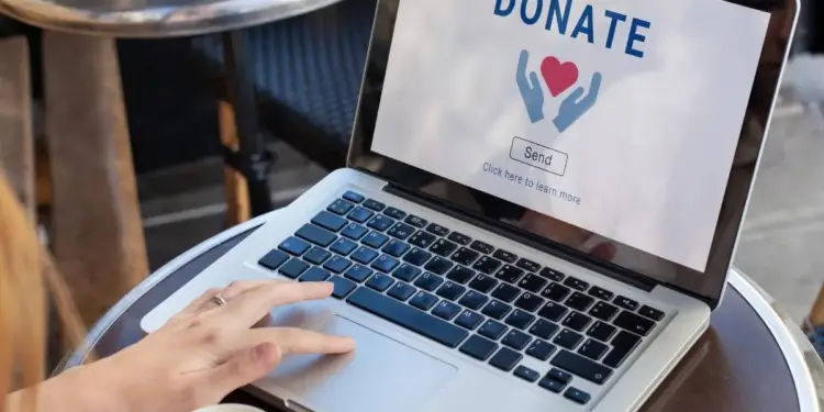 Persona utilizando un ordenador portátil en una mesa para realizar una donación online con un botón de donar en pantalla.