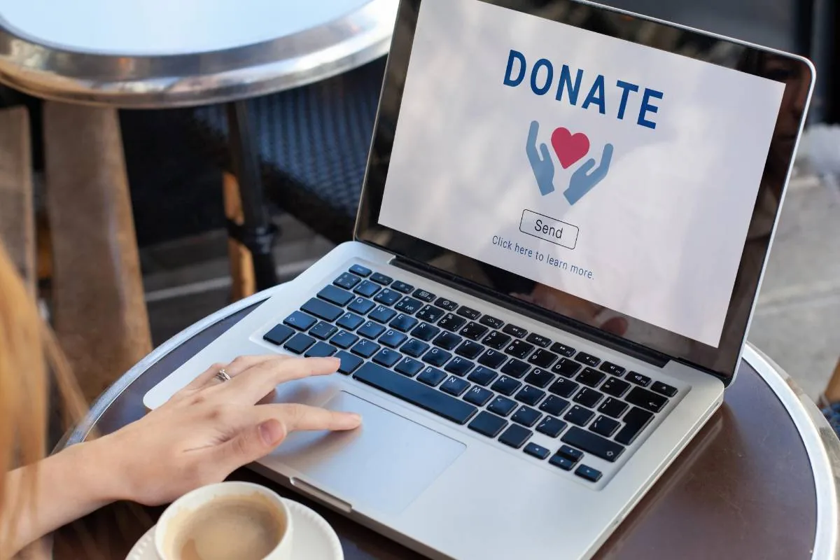 Persona utilizando un ordenador portátil en una mesa para realizar una donación online con un botón de donar en pantalla.
