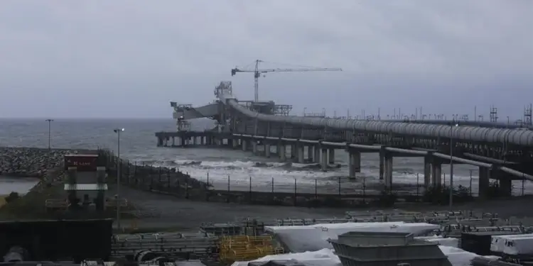 Infraestructura industrial con un largo muelle con tuberías que se extiende sobre el mar bajo un cielo nublado.